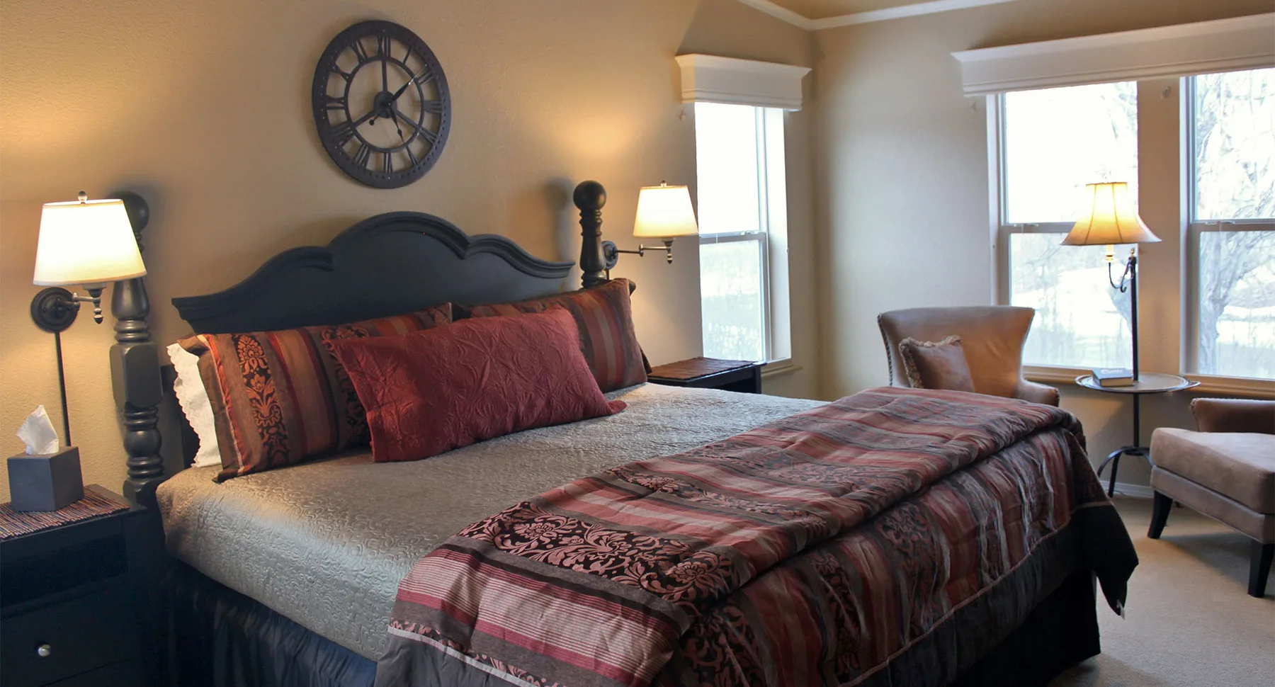Habitación con cama de postes de madera oscura, ropa de cama de color burdeos y zona de estar