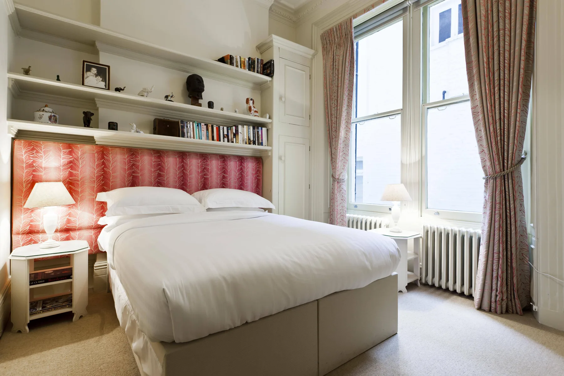 Un dormitorio con una cama bien hecha, estantes empotrados y ventanas altas con cortinas.