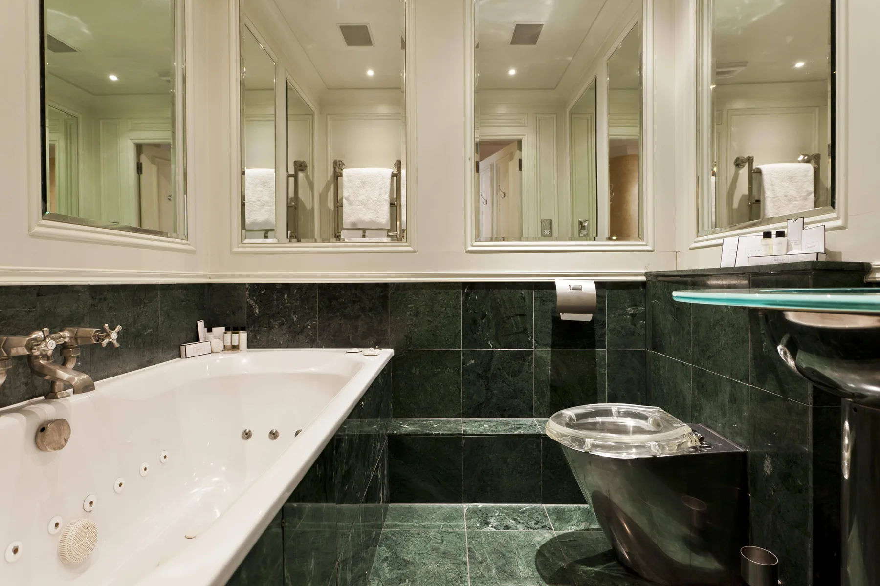 Un baño con bañera, paredes de azulejos oscuros y armarios con espejo.