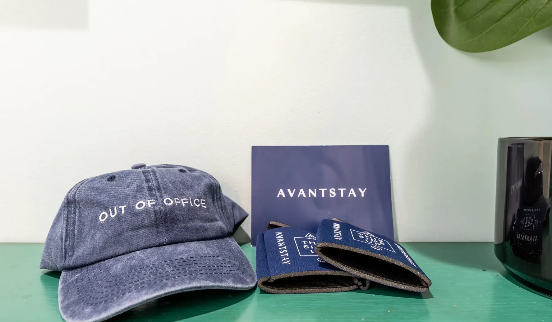 Una superficie verde exhibe una gorra, artículos impresos y un pequeño recipiente.