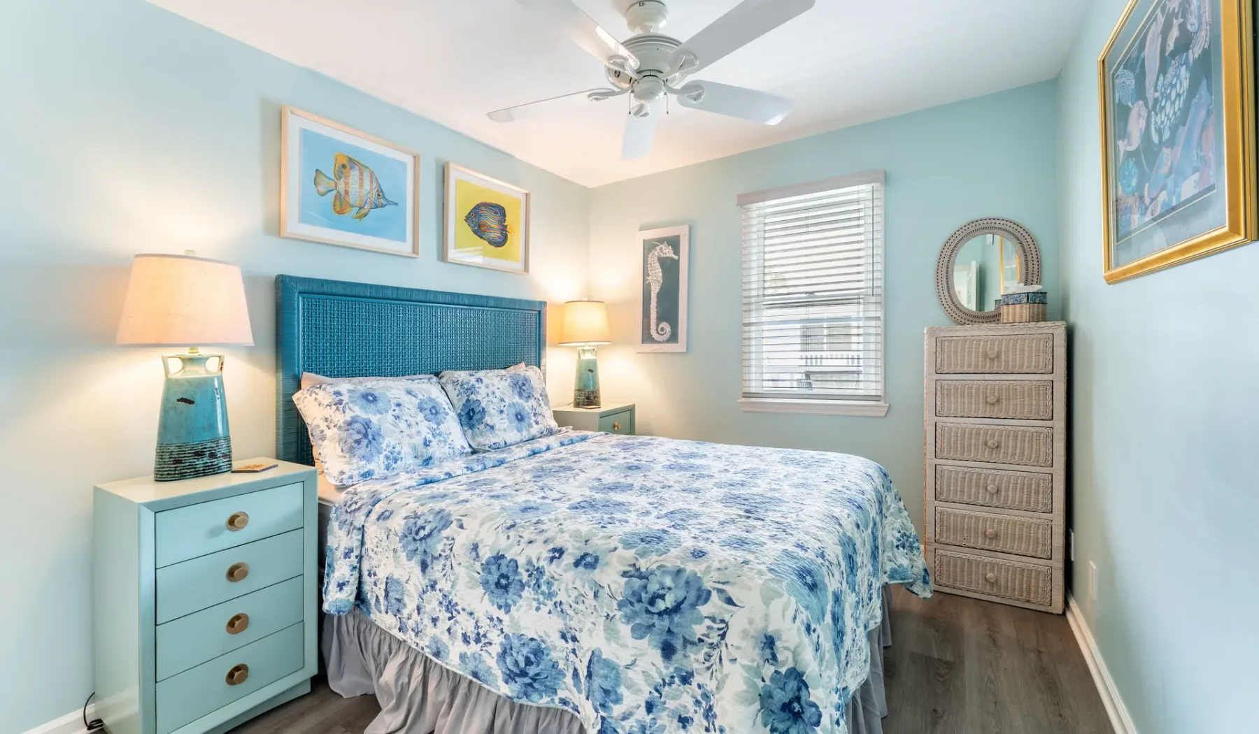 Un dormitorio con una cama azul, ropa de cama floral y un ventilador de techo.