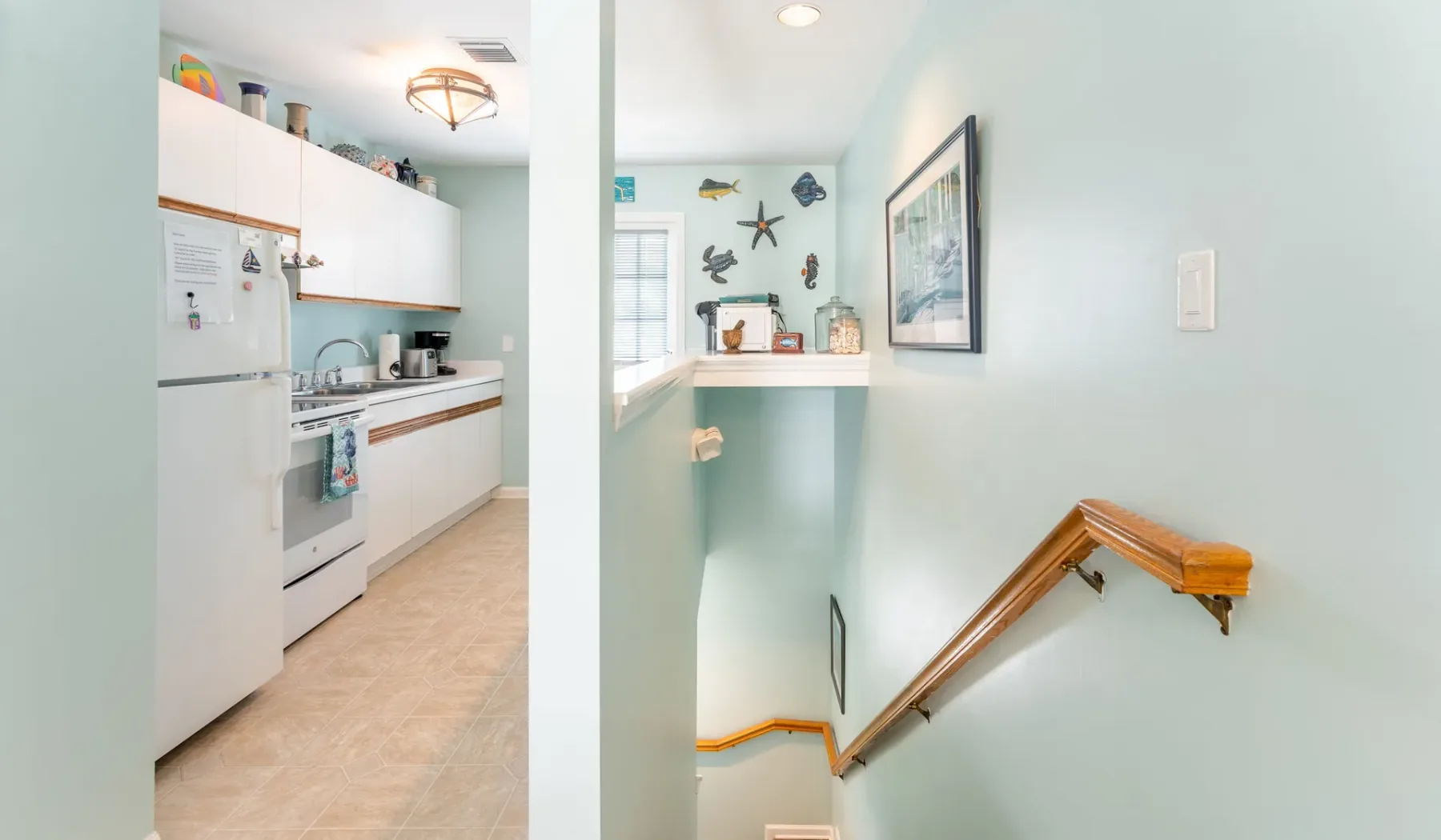 Una cocina compacta se abre a una escalera con pasamanos de madera.