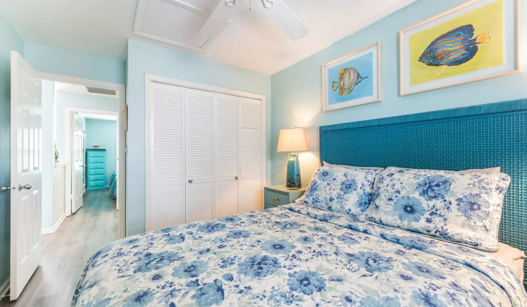 Un dormitorio con una colcha floral y cuadros de peces en la pared.