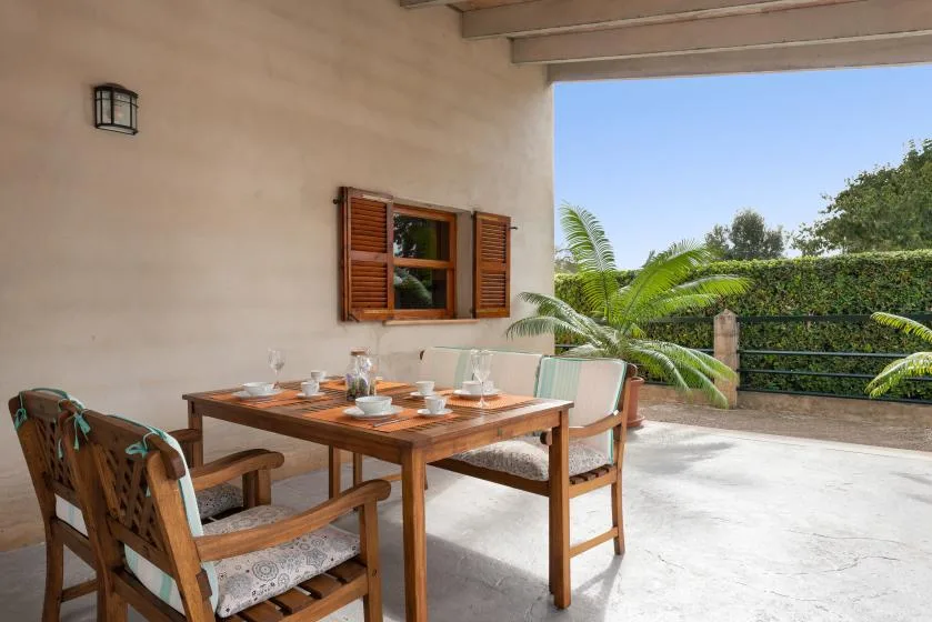 Comedor en un patio cubierto, con mesa y sillas de madera junto a plantas frondosas.
