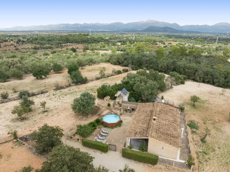 Una vista aérea muestra una casa rural rodeada de campos secos y árboles dispersos.