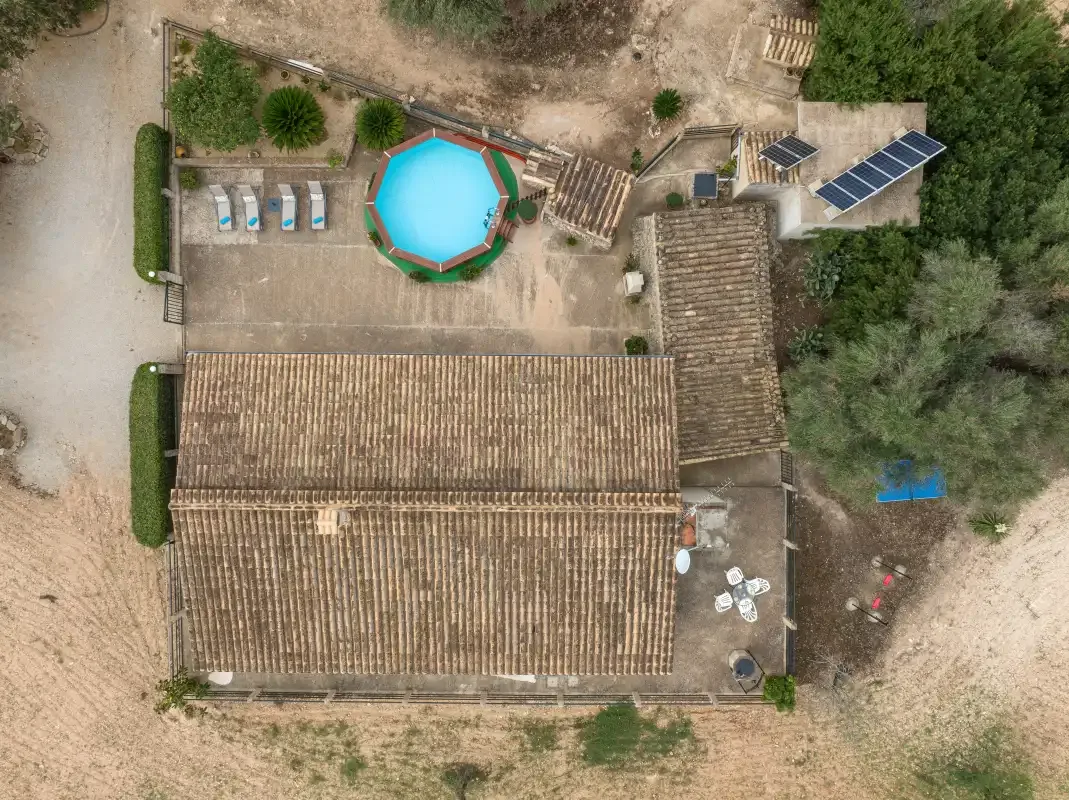 Vista aérea de un edificio con techo de tejas, una piscina y terreno alrededor.