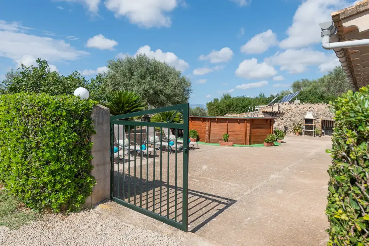 Un patio exterior pavimentado con una puerta abierta, vegetación y una cerca de madera.