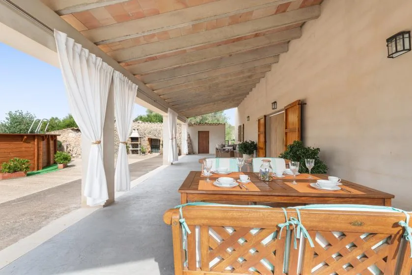 Una zona cubierta de comedor al aire libre con una larga mesa de madera puesta para comer.