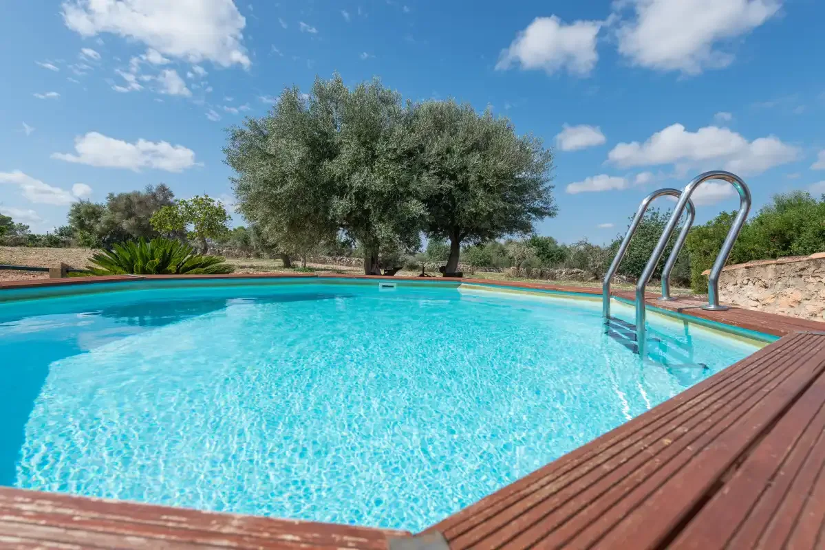 Una piscina al aire libre con una escalera metálica y árboles detrás de la terraza.
