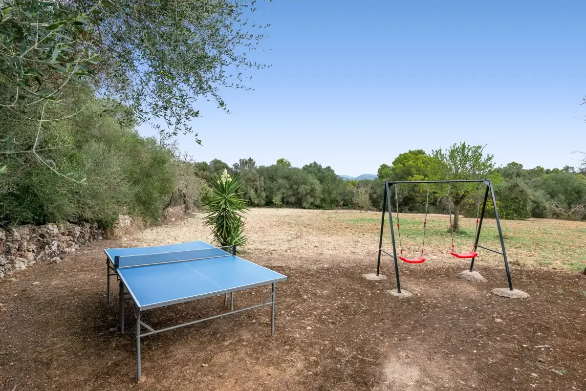 Una zona recreativa al aire libre con una mesa de ping-pong y columpios en un patio abierto y seco.
