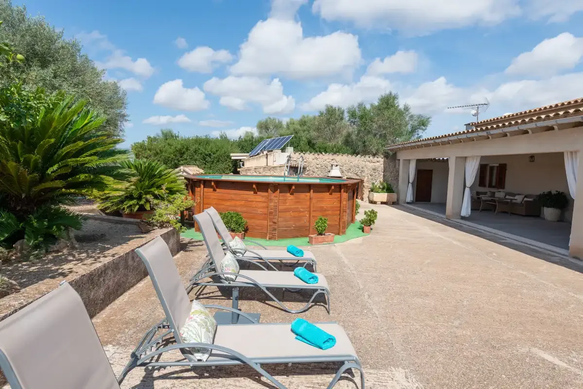 Un patio exterior tiene tumbonas junto a una bañera de hidromasaje de madera y una zona de estar cubierta.