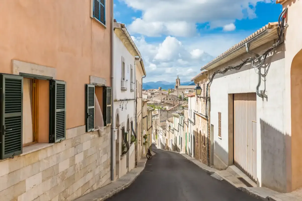 Una calle estrecha pavimentada pasa entre edificios bajo un cielo parcialmente nublado.