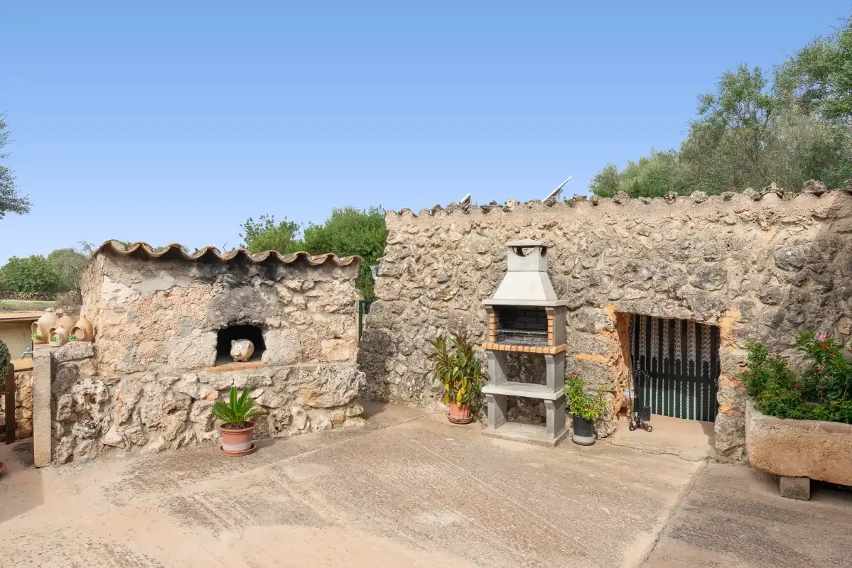 Una zona de cocina exterior de piedra con horno y barbacoa integrados.