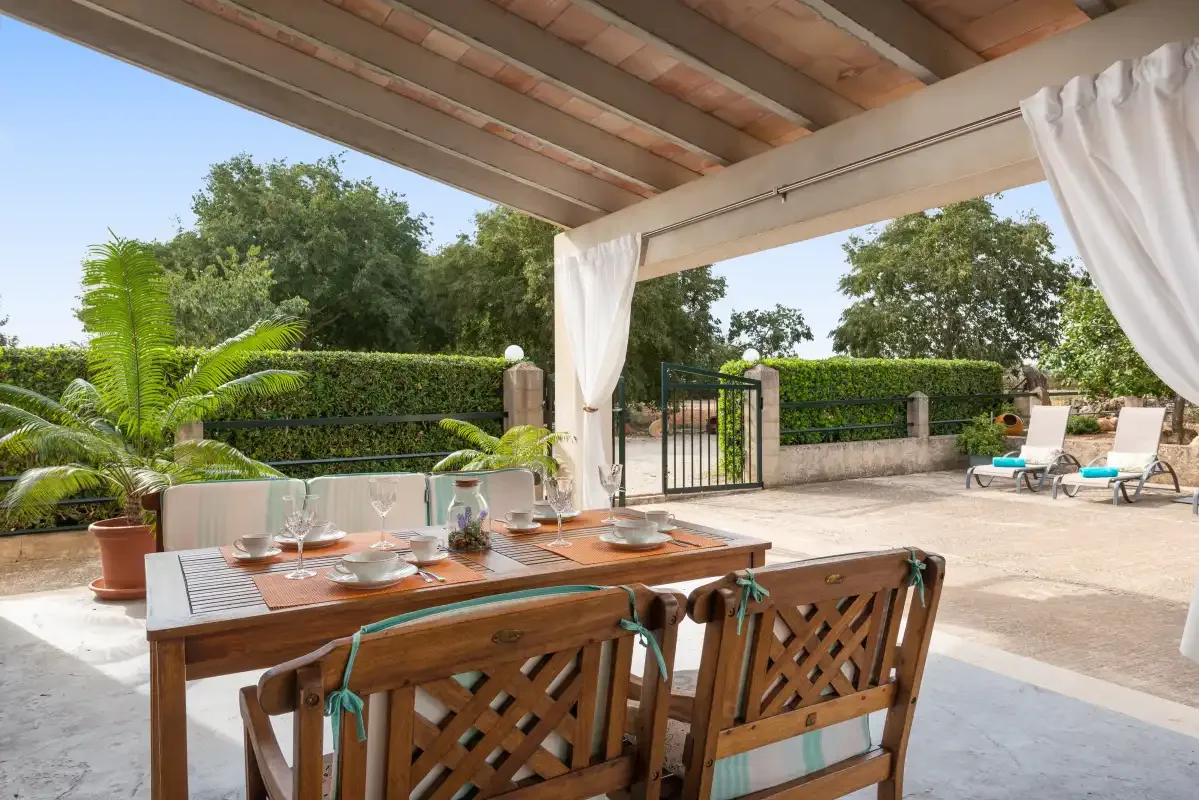Una zona cubierta de comedor exterior da a un patio pavimentado con asientos de descanso.