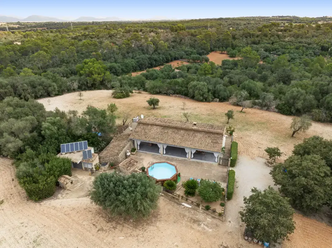 Vista aérea de una casa rural rodeada de árboles y terreno abierto.
