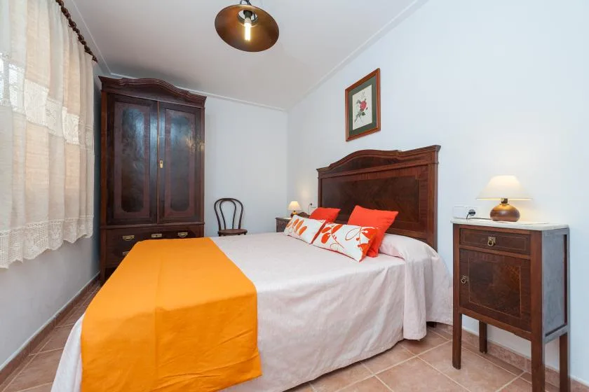 Un dormitorio con una cama grande, ropa de cama naranja y muebles de madera oscura.