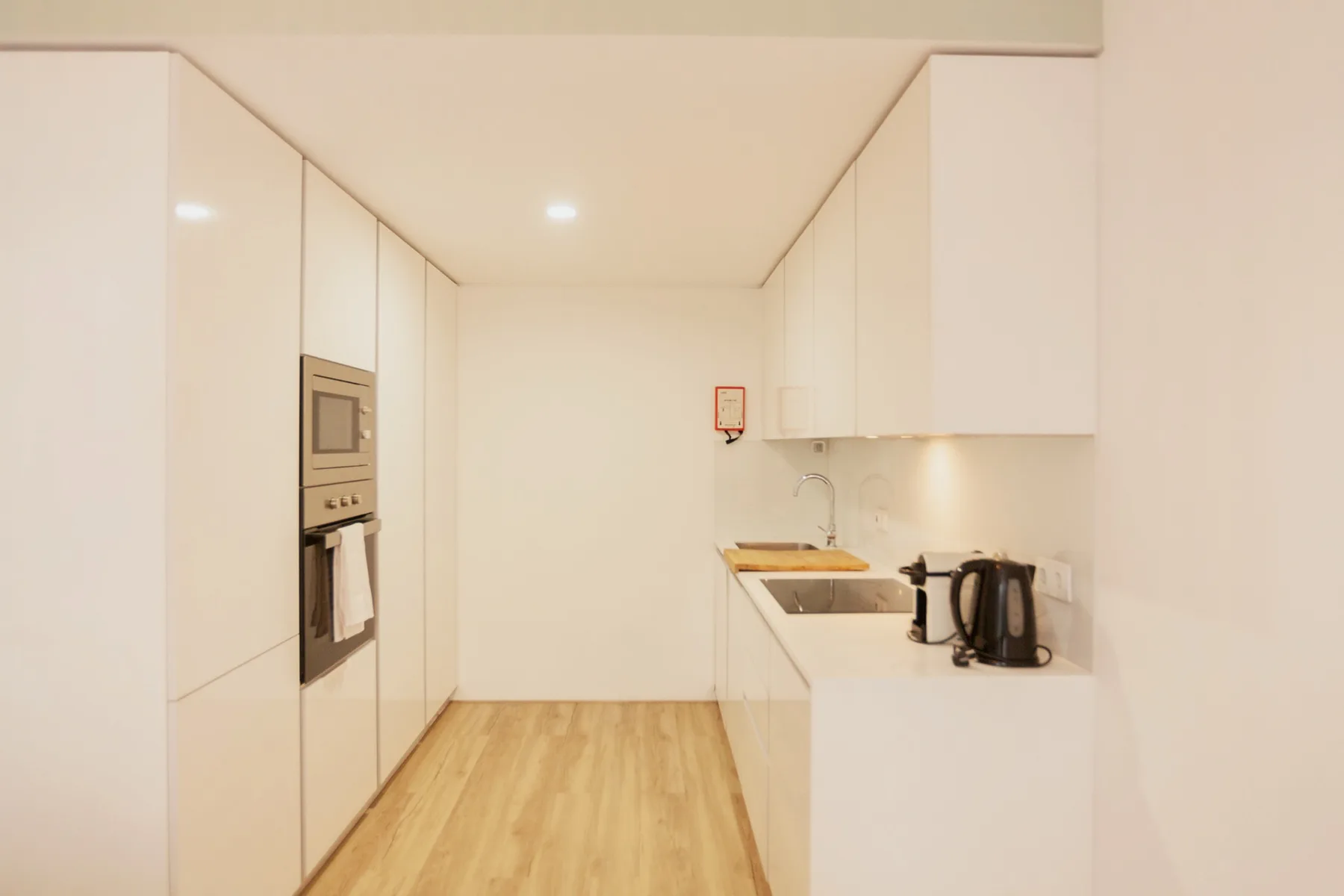 A bright modern kitchen with white cabinets, built-in appliances, and wood flooring.