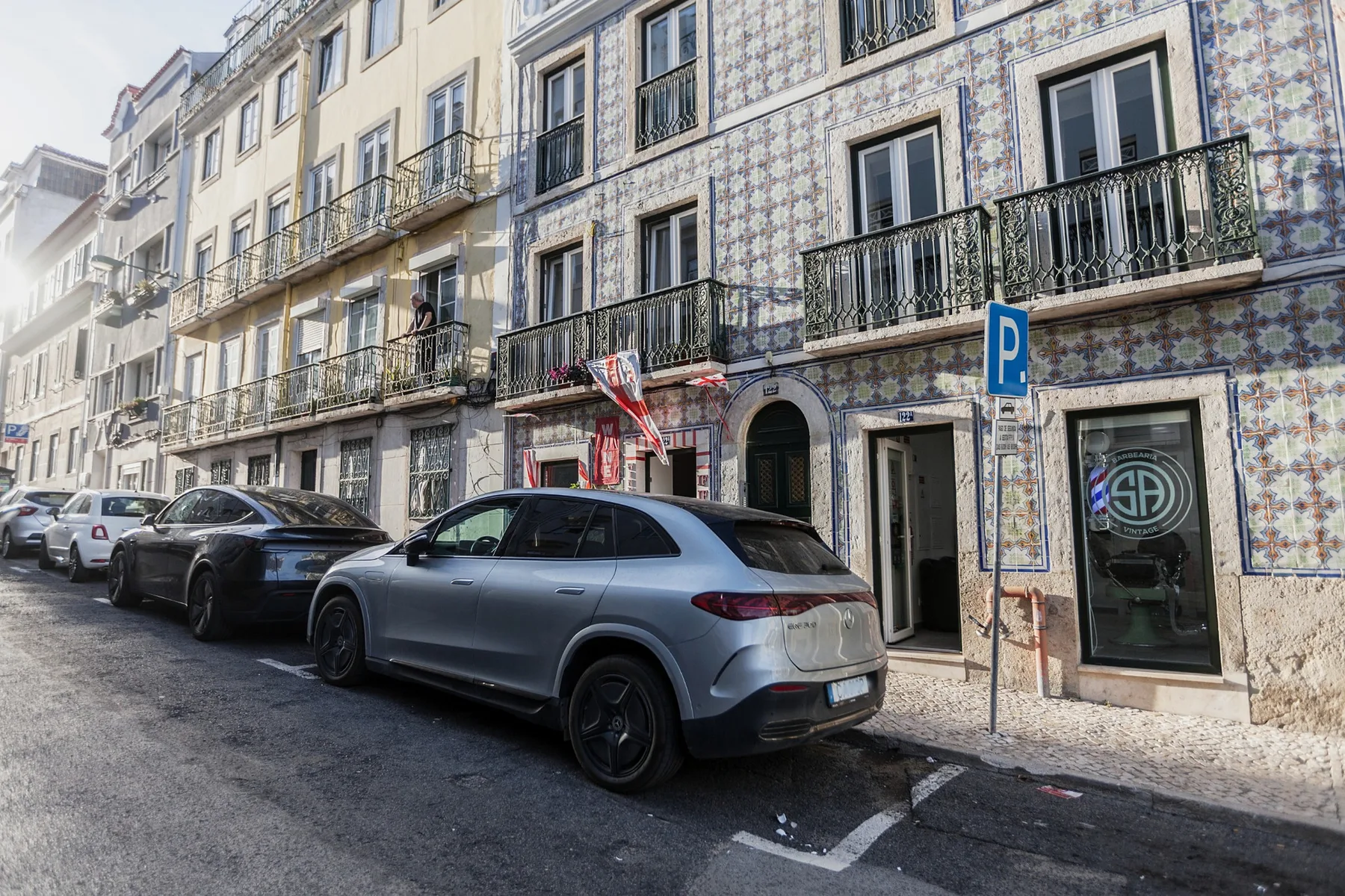 Street view of a tiled building facade with balconies and parked cars.