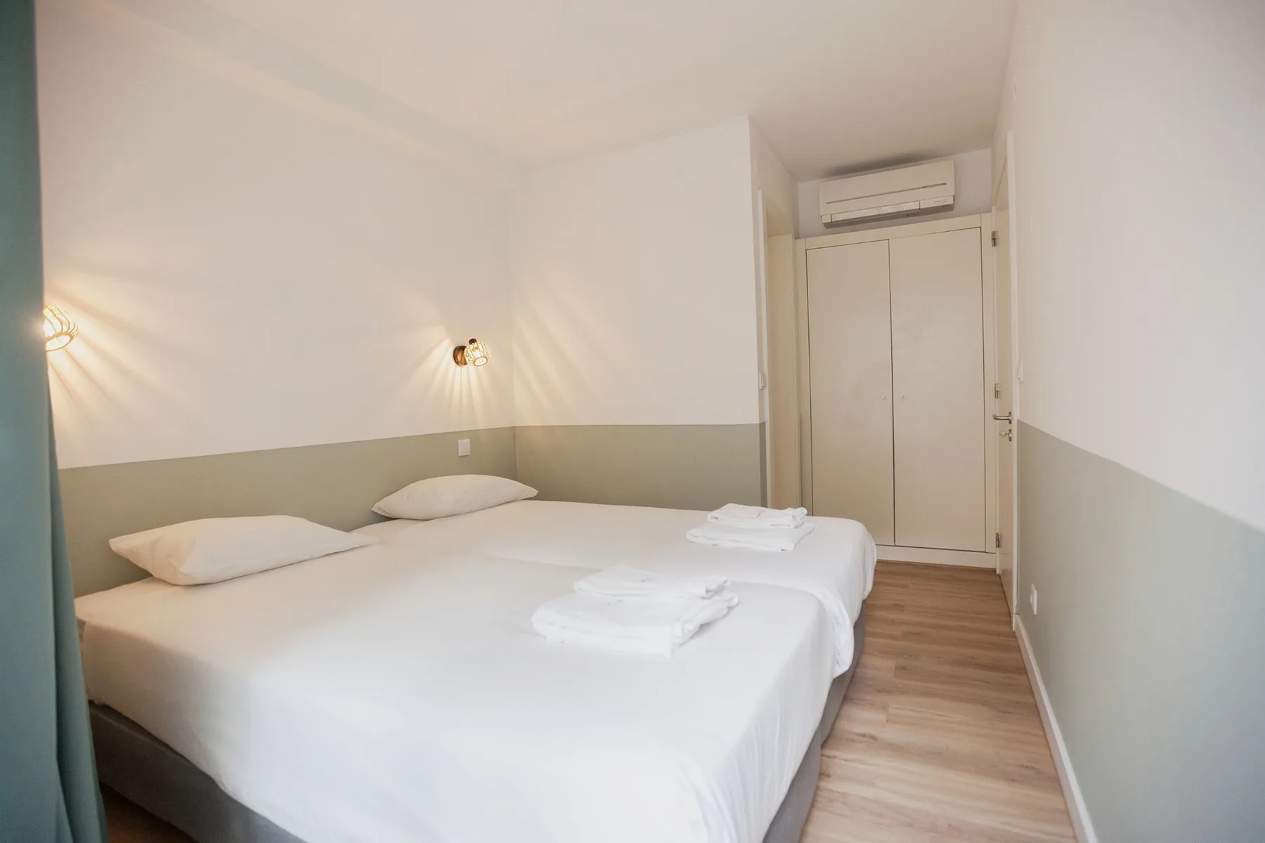 A bedroom with two beds, folded towels, and a wall-mounted air conditioner.