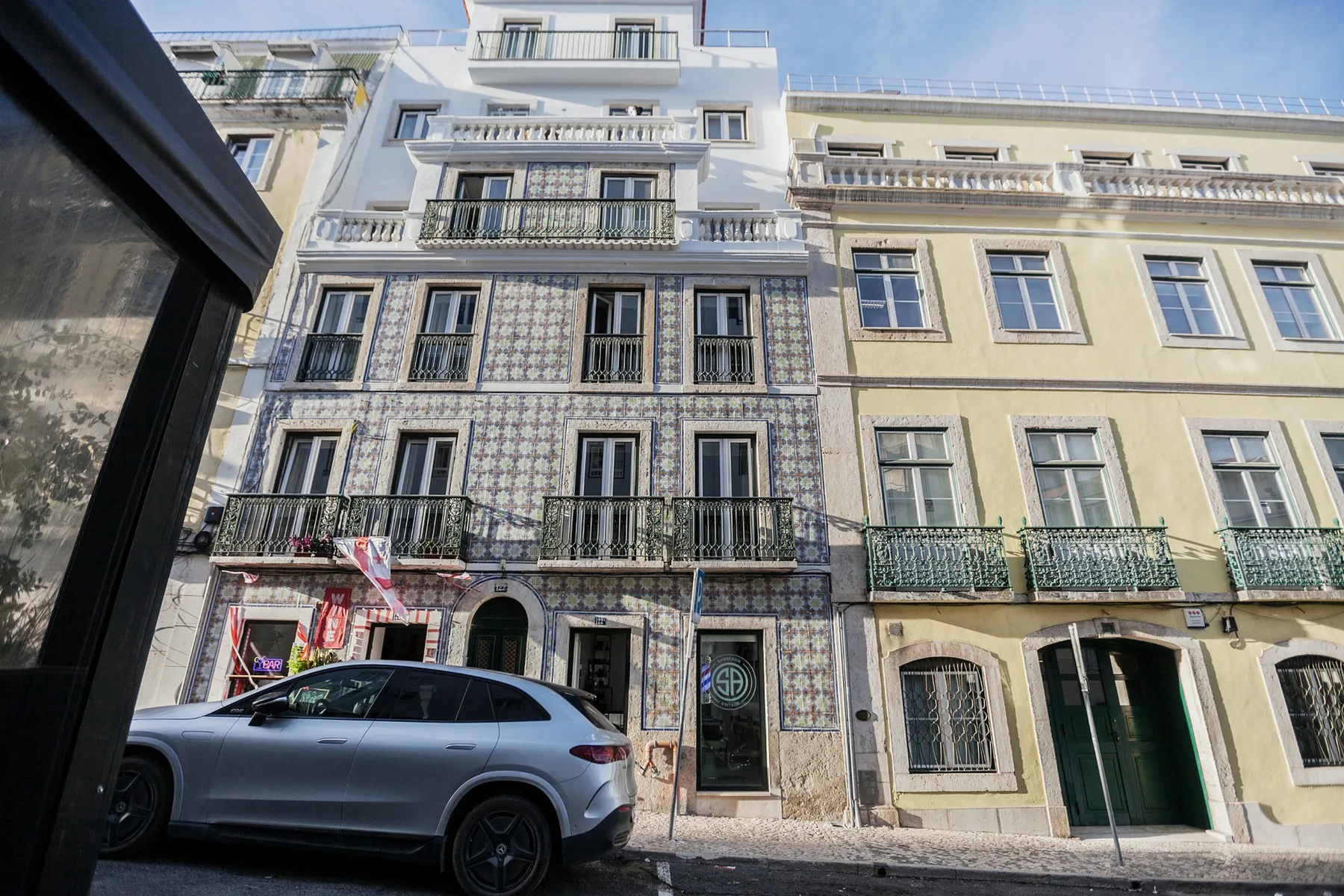 A tiled apartment building facade with balconies faces a city street.