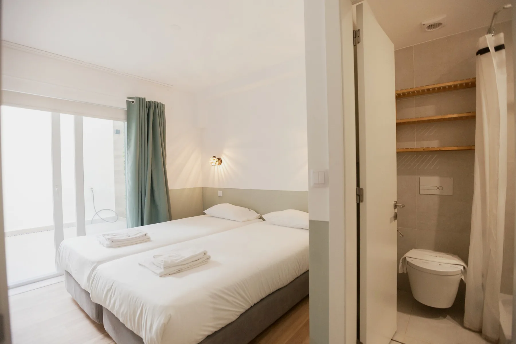 A bright bedroom with a neatly made bed beside an open bathroom.