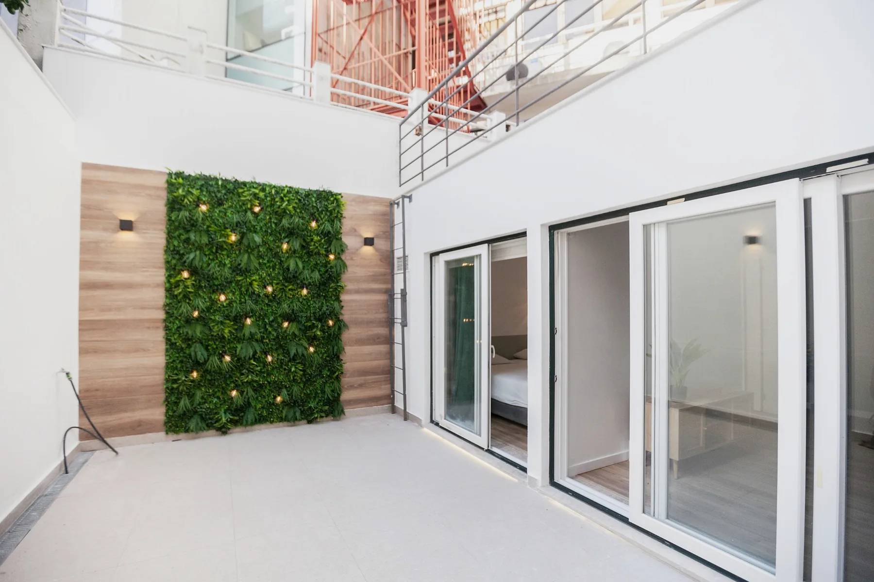A bright terrace with a green plant wall and glass doors.