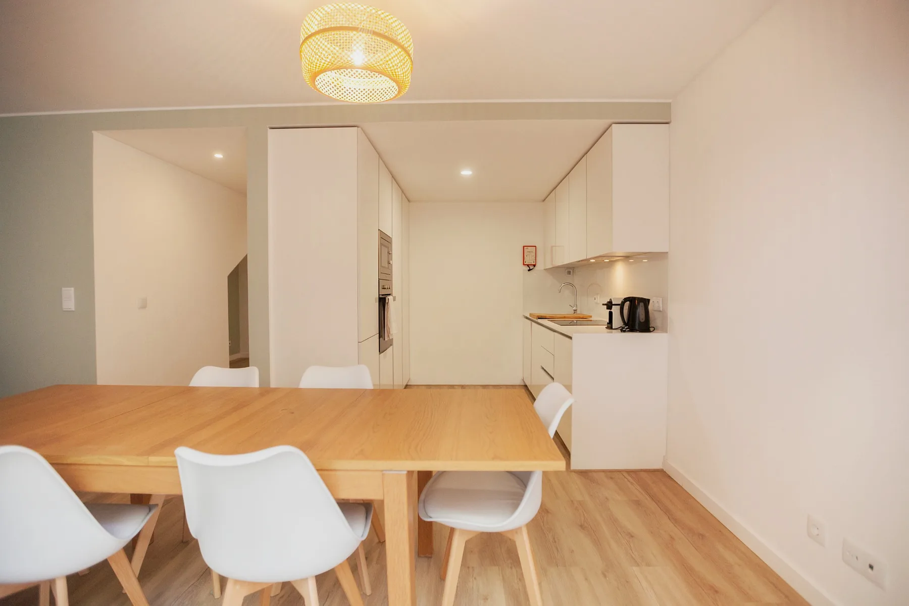 A dining area with a wooden table and white seating beside a compact kitchen.