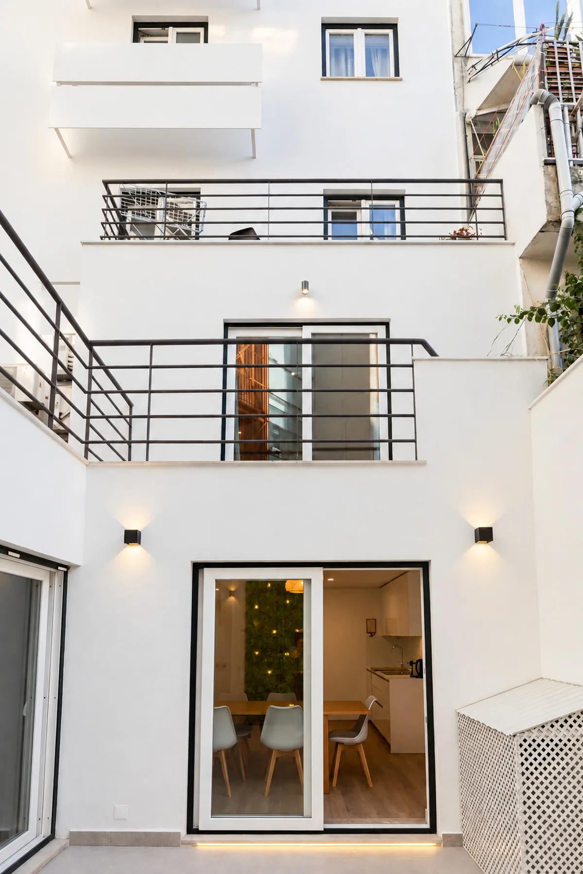 A white multi-level building facade with balconies and large glass doors opening onto a dining area.