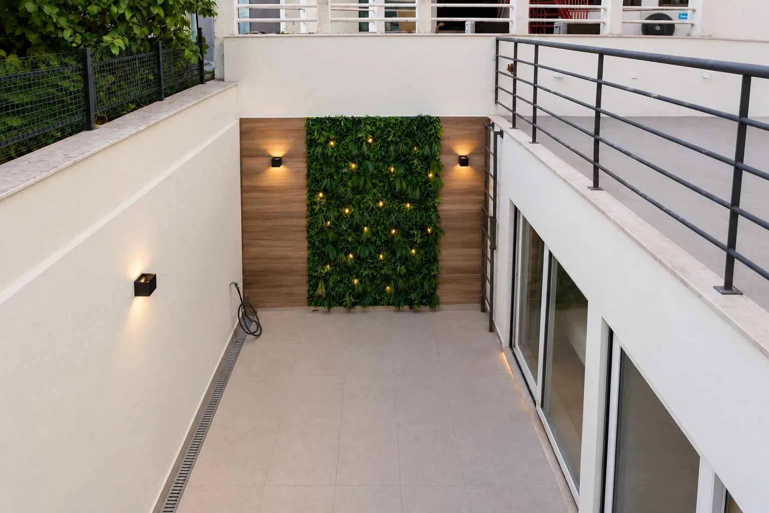 A sunken outdoor patio with a green plant wall and surrounding railings.