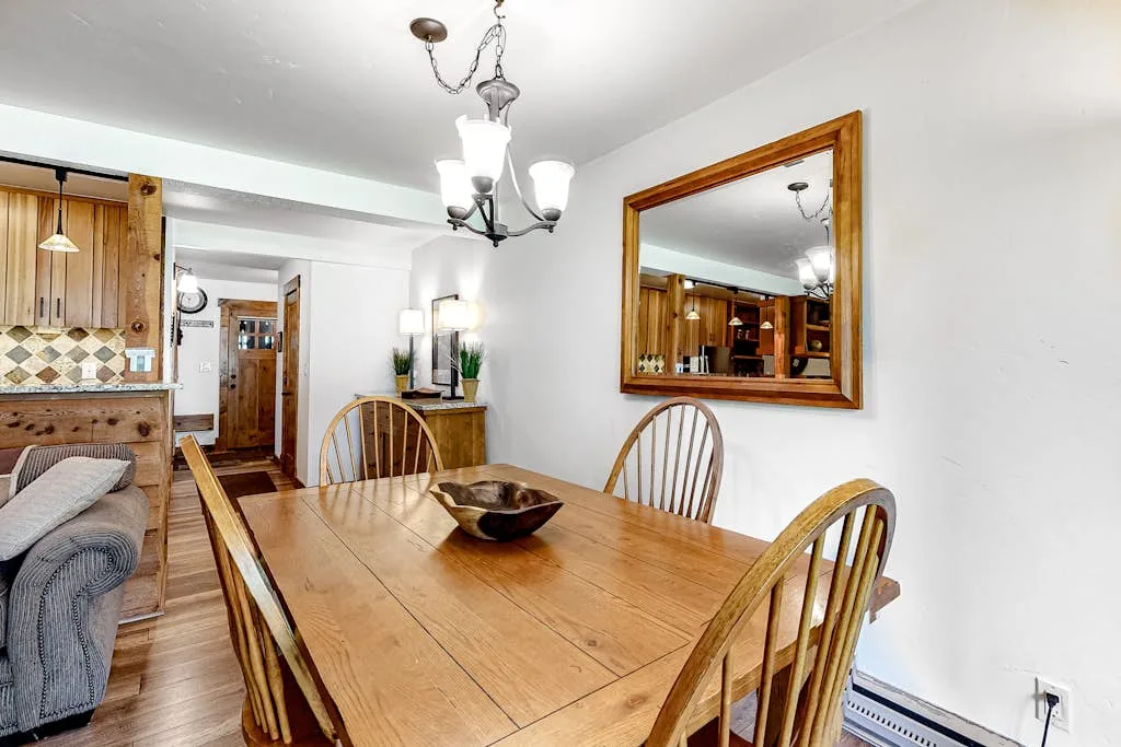 A wooden dining table and chairs sit beside a kitchen with wood cabinetry.