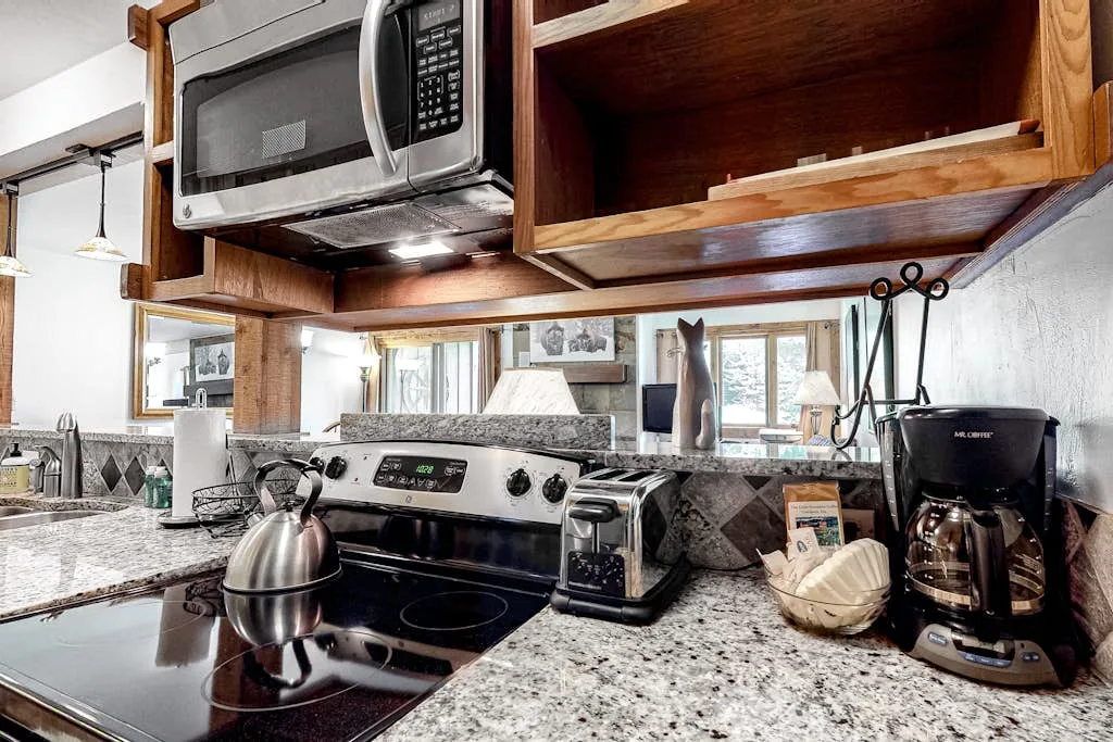 A kitchen with a stovetop, countertop appliances, and wooden cabinets.