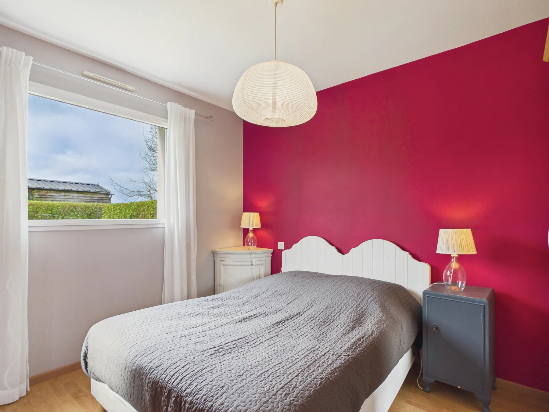 A bedroom with a bed against a bright red accent wall and a window.