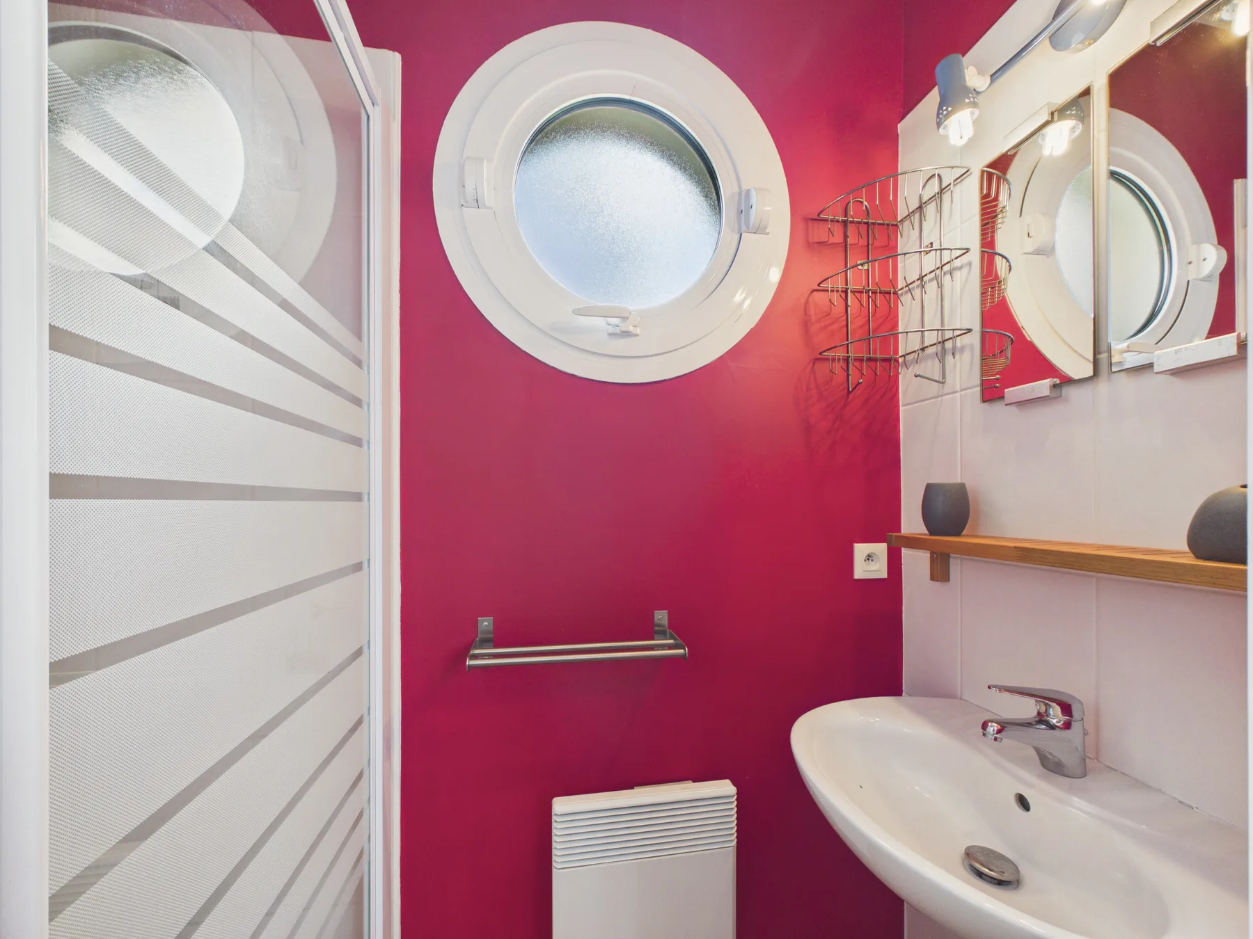 A bathroom with a wall-mounted sink, round window, and red walls.