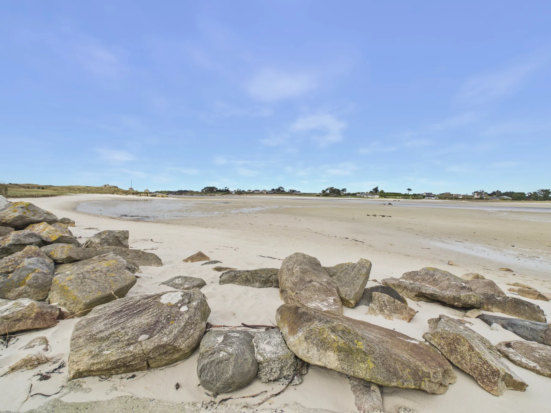 A sandy beach stretches across a broad tidal flat, with rocks in the foreground.