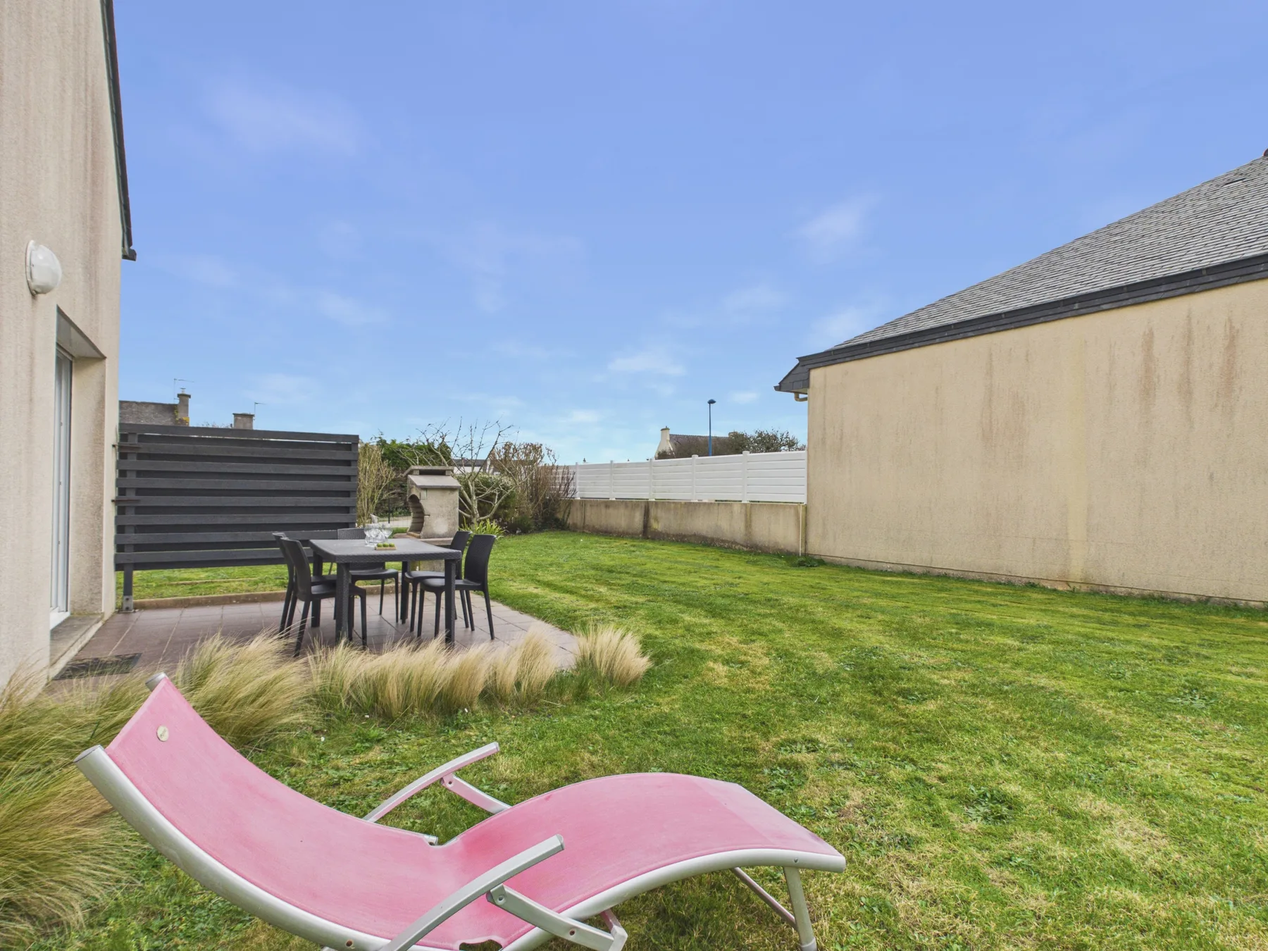 A grassy backyard with patio seating and a pink lounge chair.