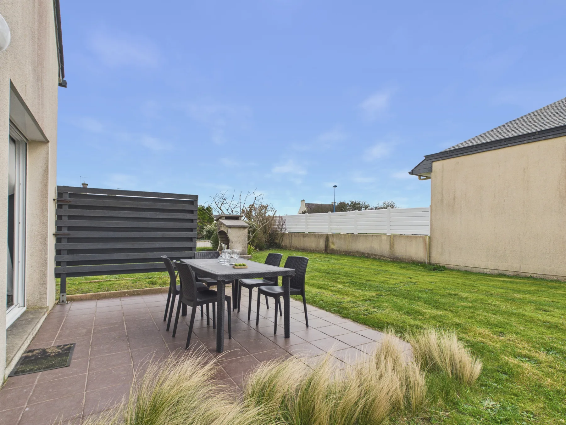 A patio dining area beside a lawn, with outdoor seating and a table.