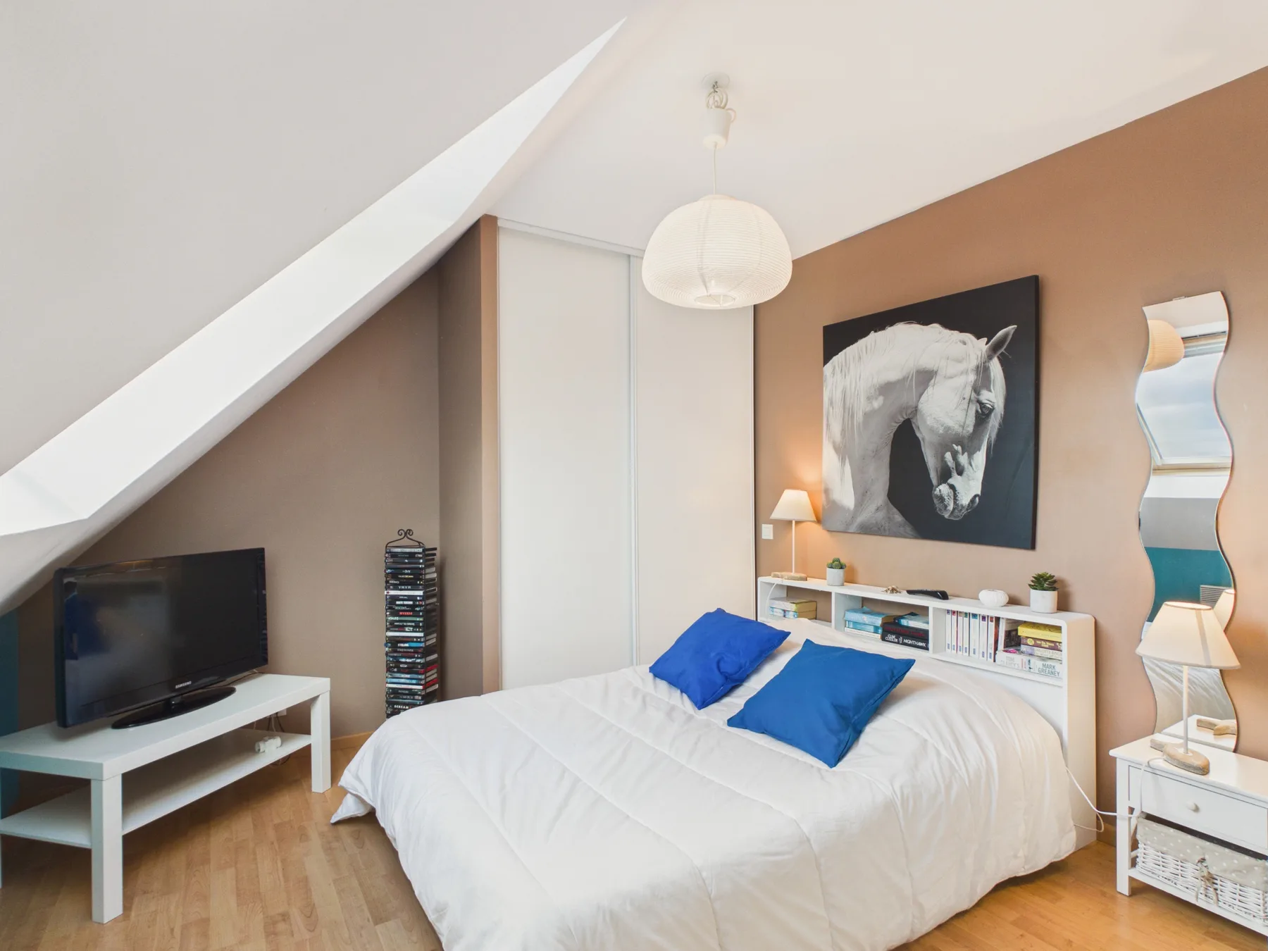A bedroom with a bed, television, and horse artwork on the wall.