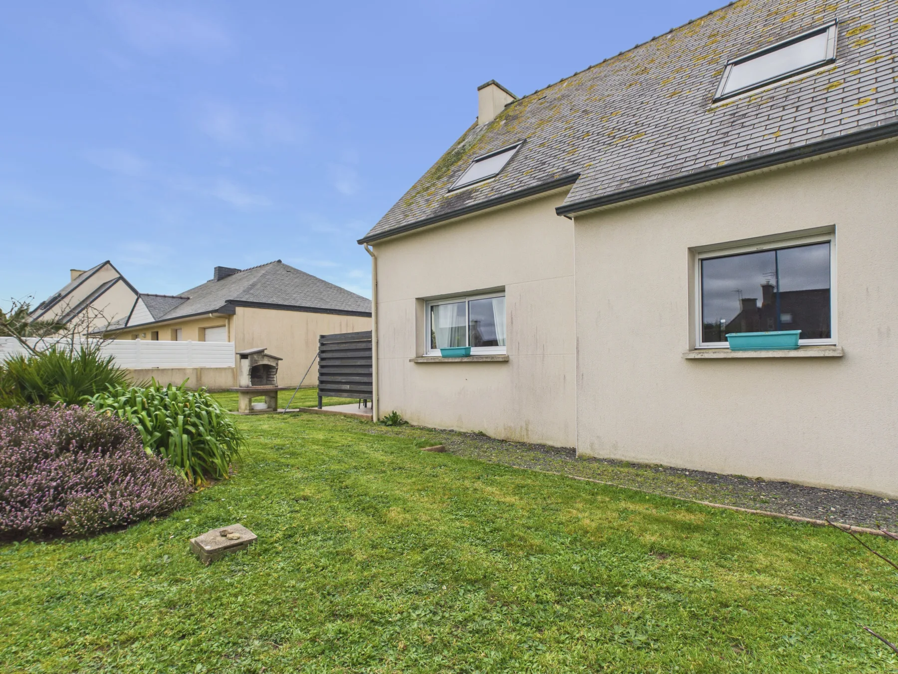 A house with a sloped roof stands beside a grassy garden.