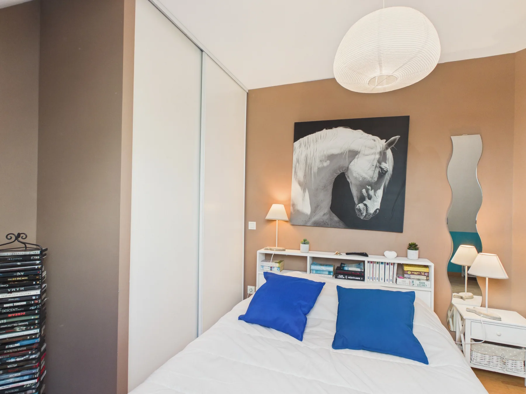 A bedroom with a bed, blue pillows, and a horse portrait on the wall.