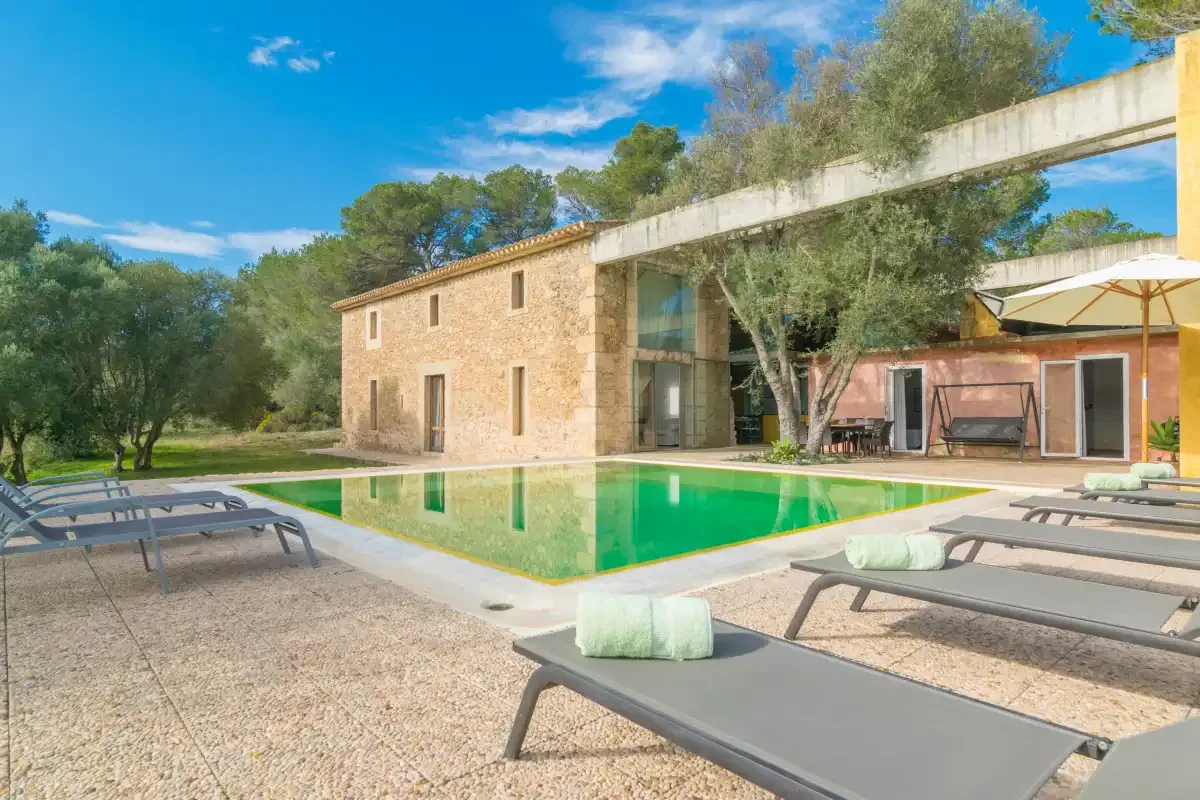 Una piscina y asientos reclinables están junto a una casa de piedra al aire libre.