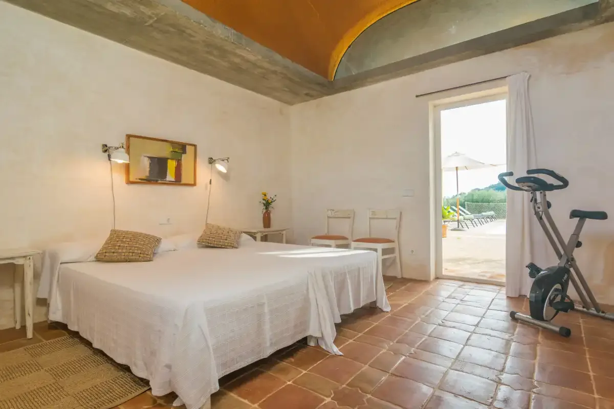 Dormitorio con una cama grande y una bicicleta estática junto a la puerta abierta.