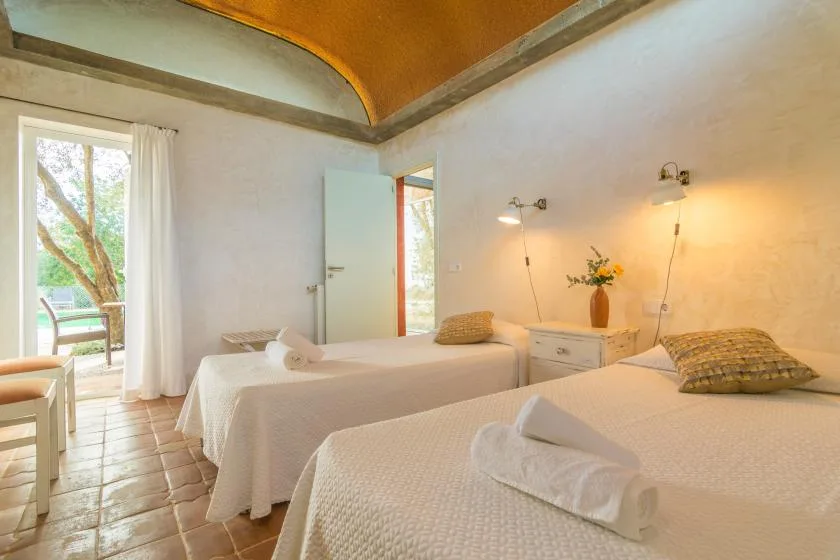 Un dormitorio luminoso con dos camas, mesitas de noche y una puerta que da a un balcón.