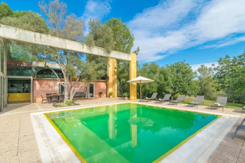 Una piscina al aire libre junto a un edificio moderno, con asientos y una sombrilla.