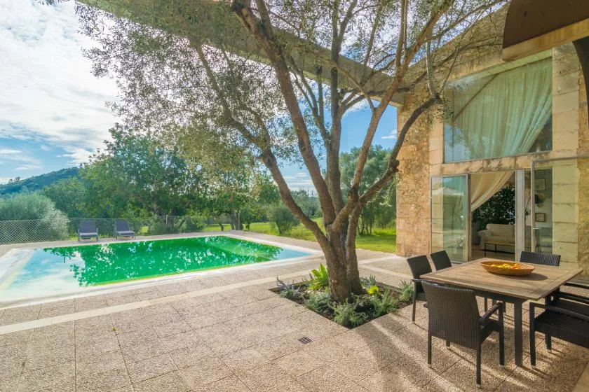 Una piscina y una zona de comedor al aire libre están junto a una casa acristalada.
