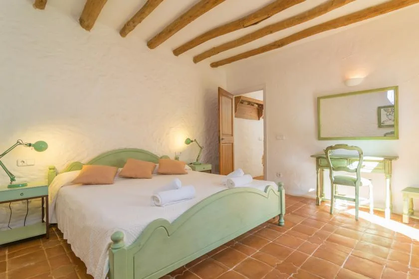 Un dormitorio con una cama verde, mesitas de noche y vigas expuestas en el techo.