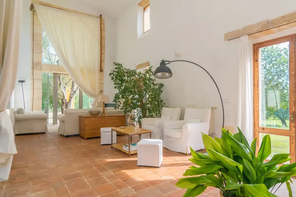 Una sala de estar luminosa con asientos blancos, una mesa de centro y grandes ventanales.