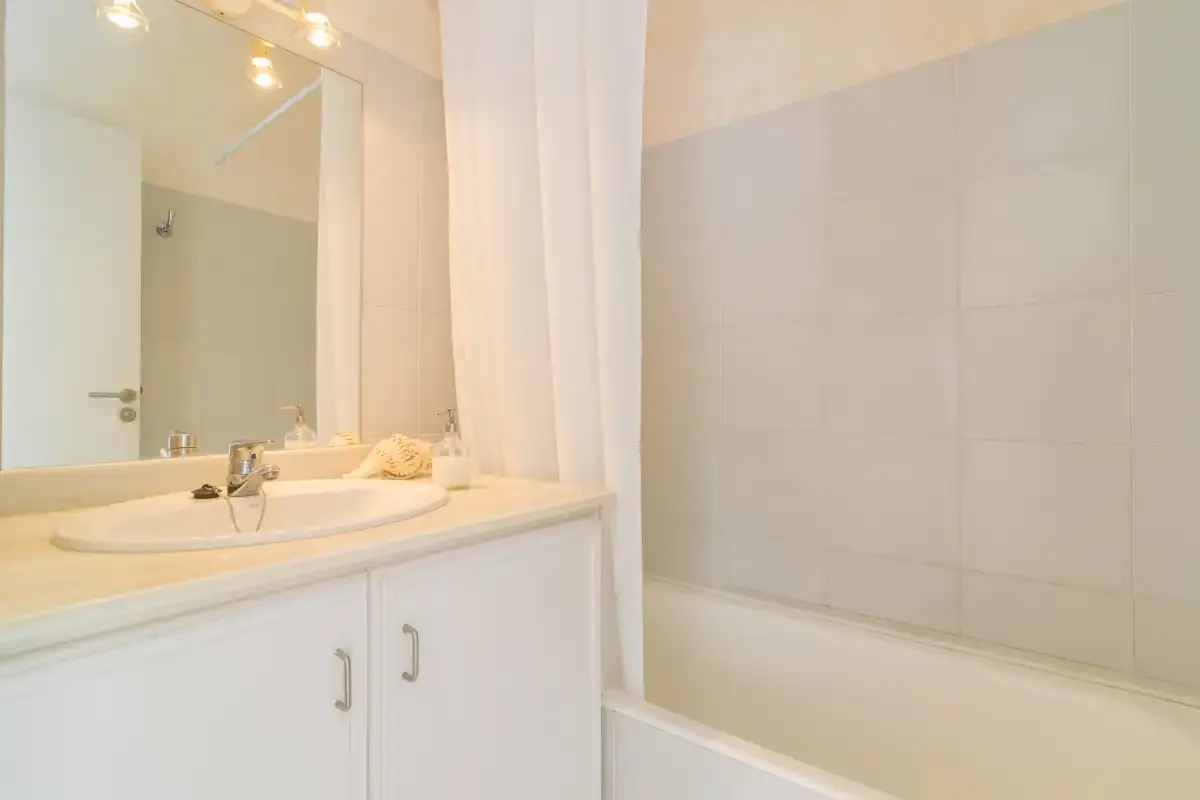 Un baño con lavabo, espejo y bañera detrás de una cortina.