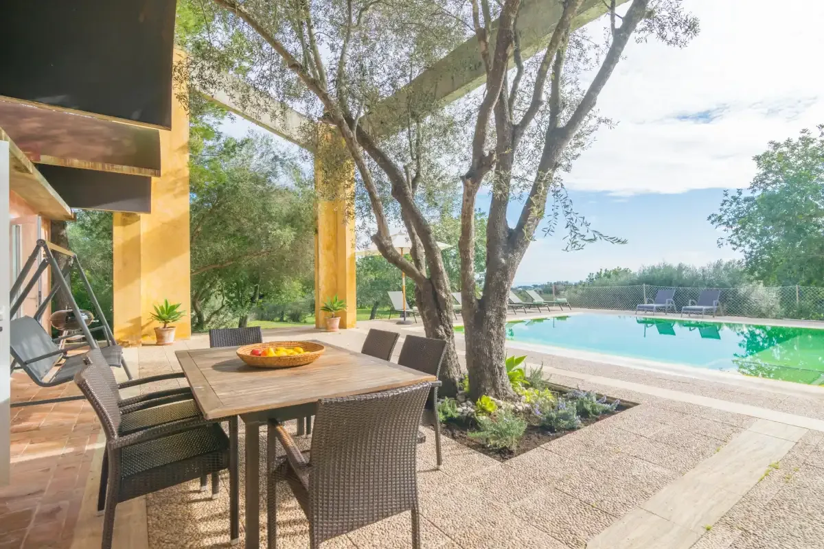 Una zona de comedor exterior a la sombra da a una piscina y un jardín.