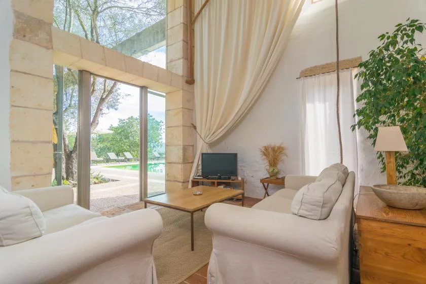 Una sala de estar luminosa con asientos claros y grandes ventanas con vistas a la vegetación.
