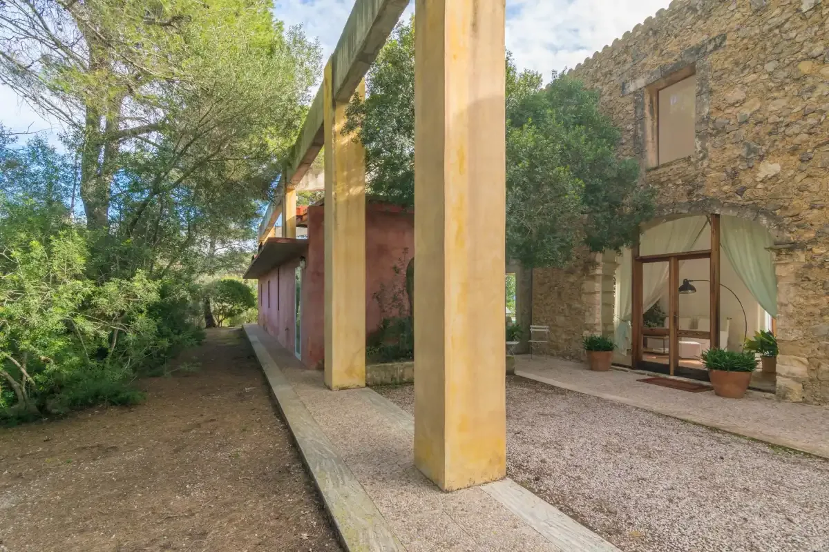 Un patio junto a un edificio de piedra, con un pasillo cubierto y árboles alrededor.